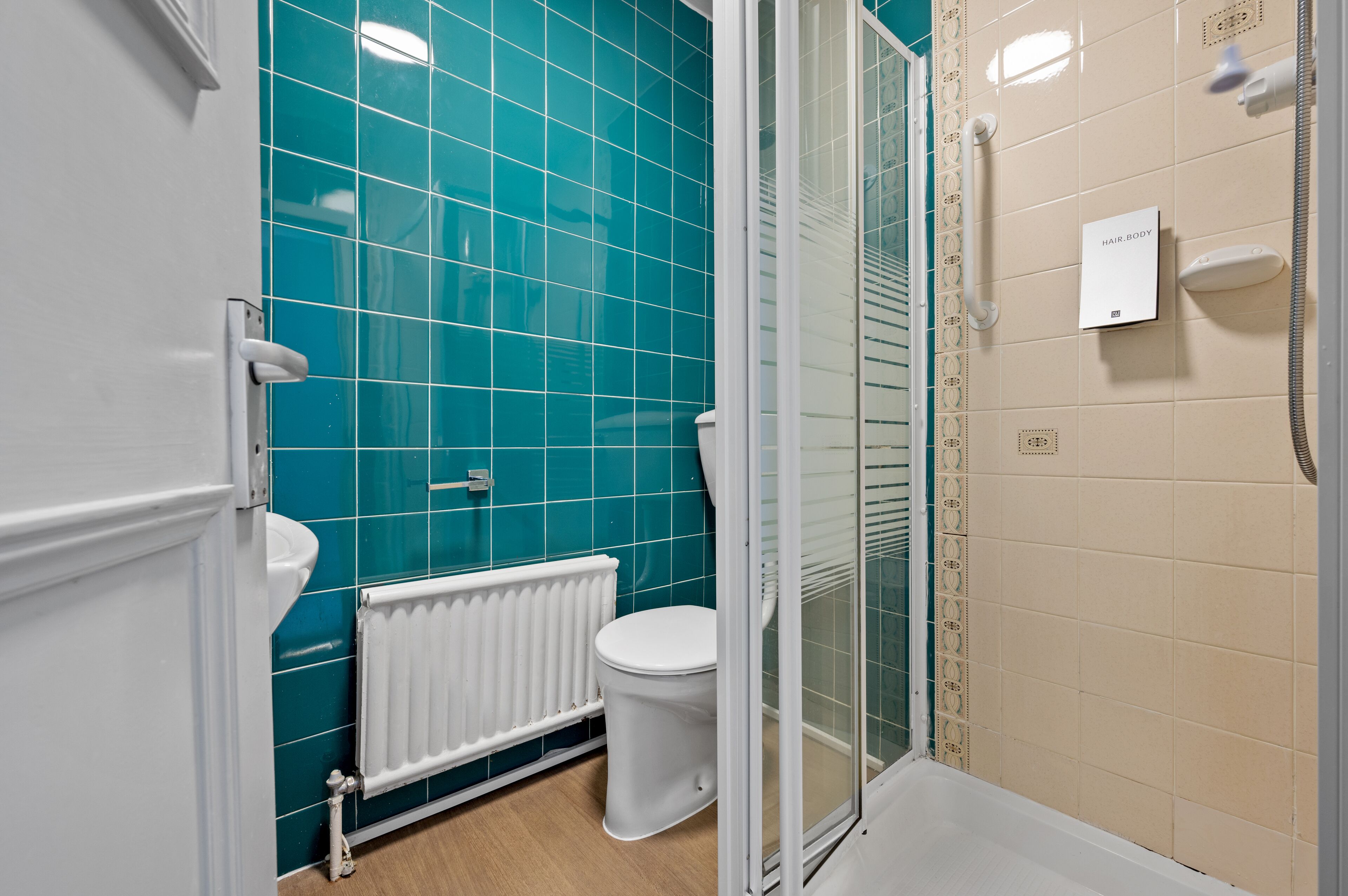 Un baño con azulejos color turquesa, un inodoro blanco, un radiador blanco y una zona de ducha con puerta de cristal.