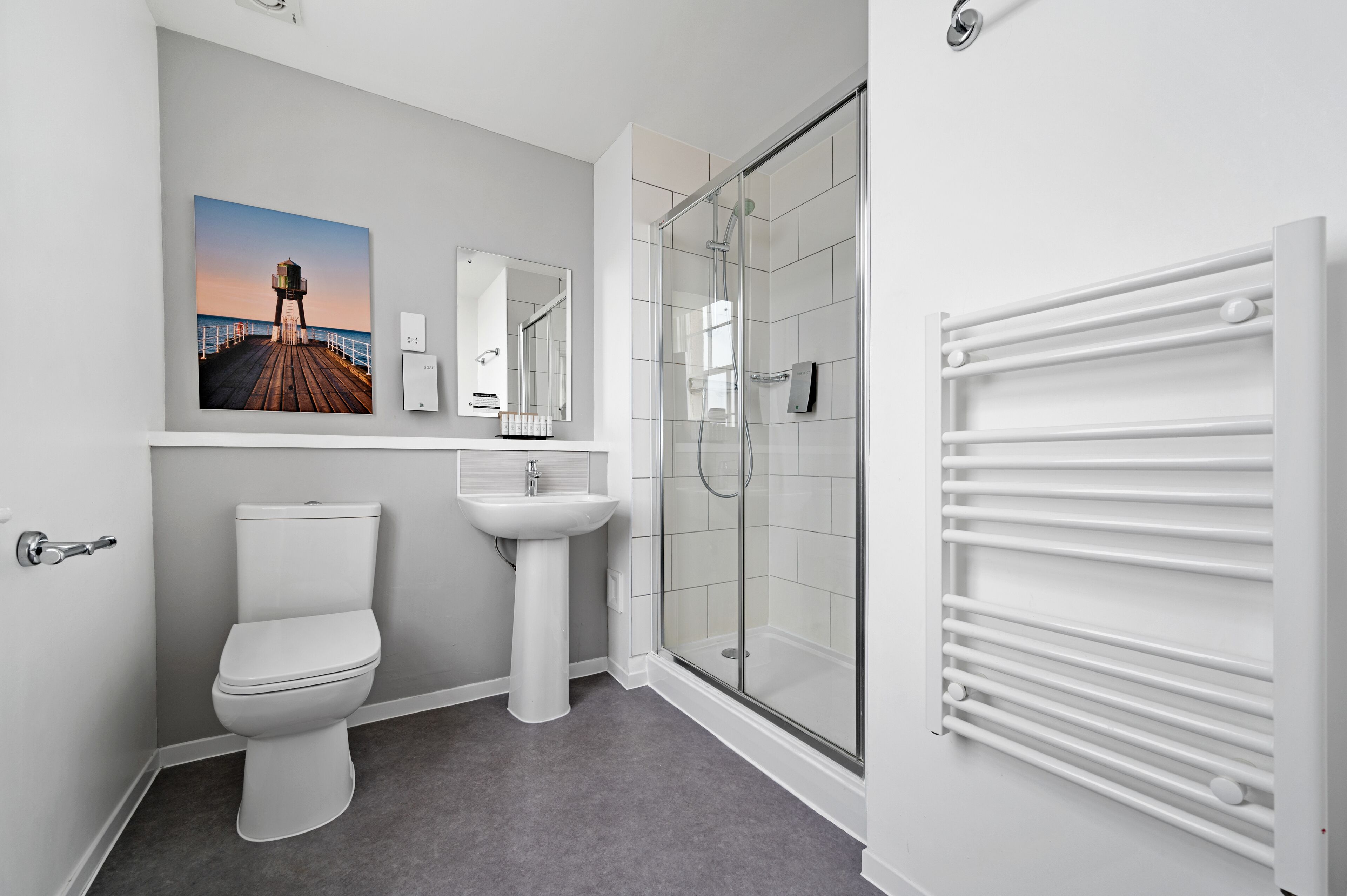 Et moderne badeværelse med toilet, vask og glasvæg omkring bruseren.