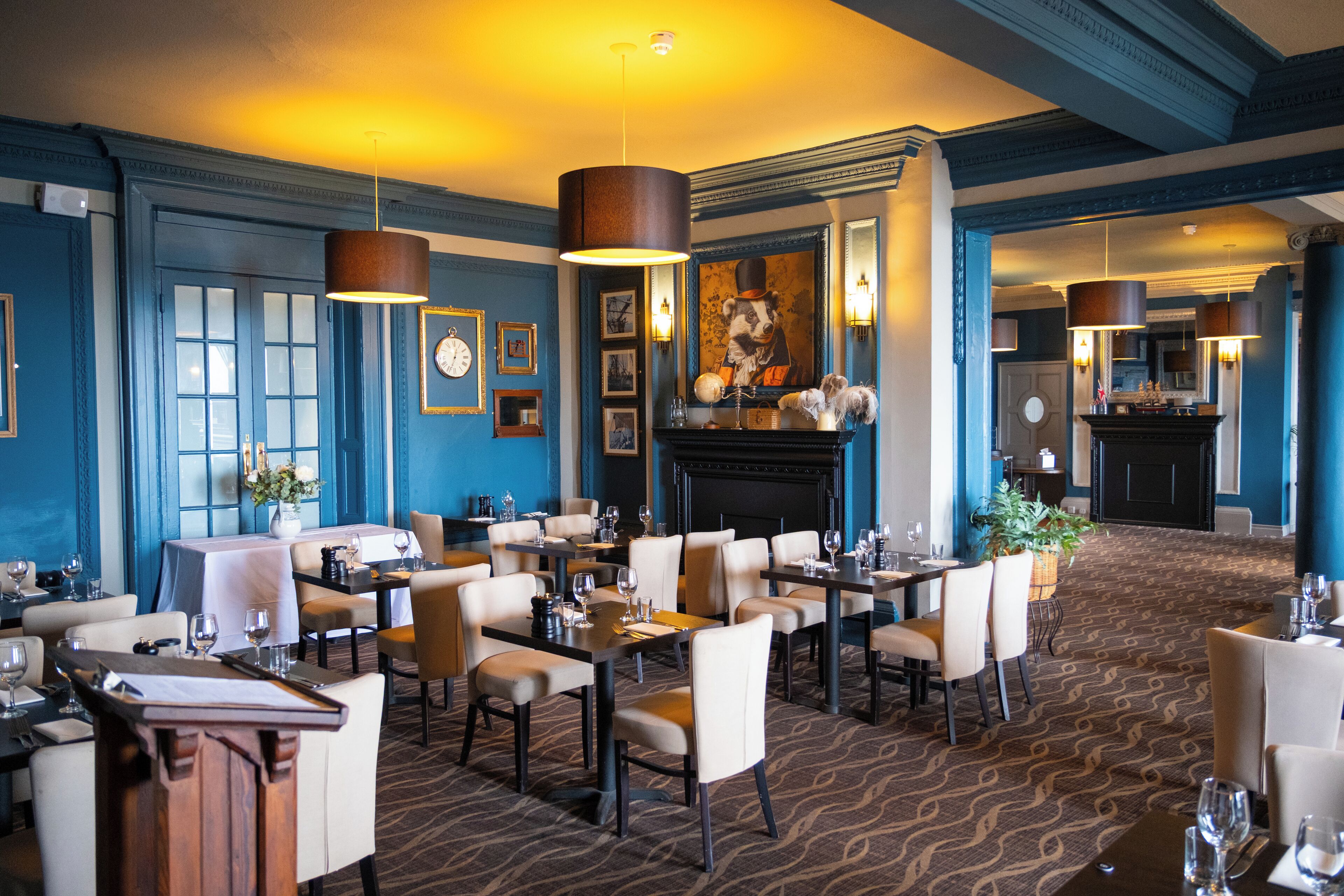 A restaurant with a blue and beige color scheme, featuring a fireplace, multiple dining tables, and a large painting on the wall.