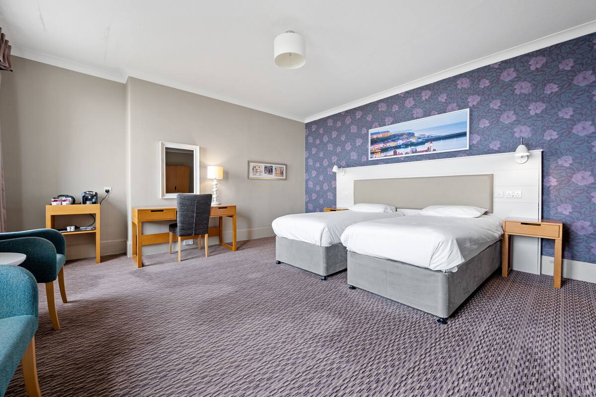 A hotel room with two beds, a desk, a chair, and a small table.