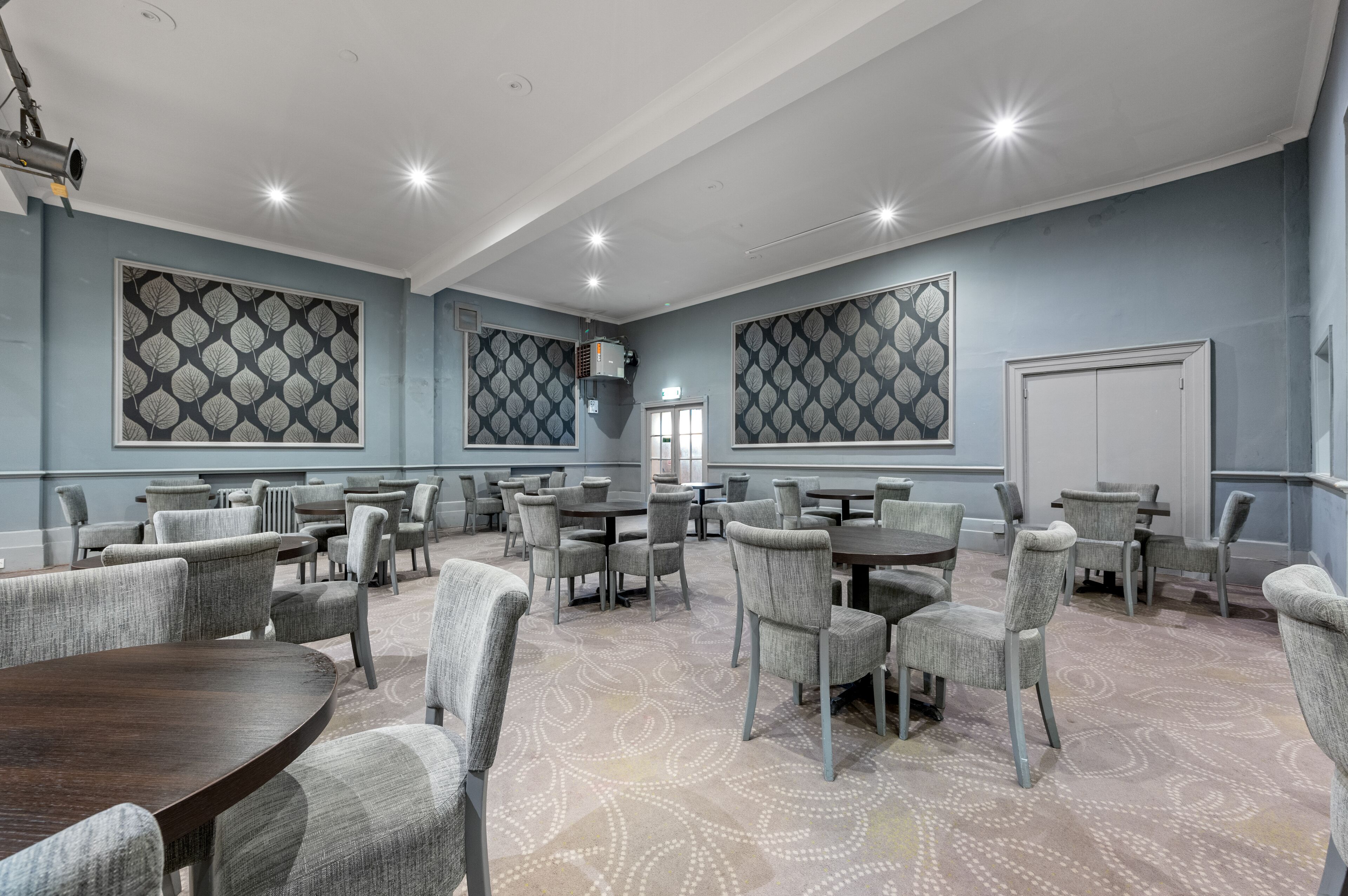 A conference room with multiple tables and chairs, large patterned wall decorations, and a whiteboard.