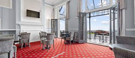 A room with a red carpet, grey chairs, a table, and large windows offering a view of the sky and a parked car outside.