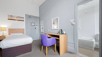 Quarto de hotel com cama, escrivaninha com cadeira, chuveiro e um quadro na parede.
