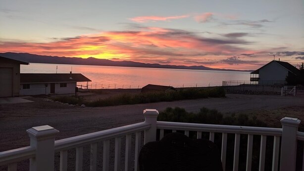 A sunset view from a porch with a railing, overlooking a body of water and distant mountains. - Right by the lake and fast walk to the beach.  (Saint Charles)