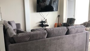 A modern living room with a grey sofa, a flat-screen TV mounted on the wall, and a guitar leaning against the wall. - Right by the lake and fast walk to the beach.  (Saint Charles)