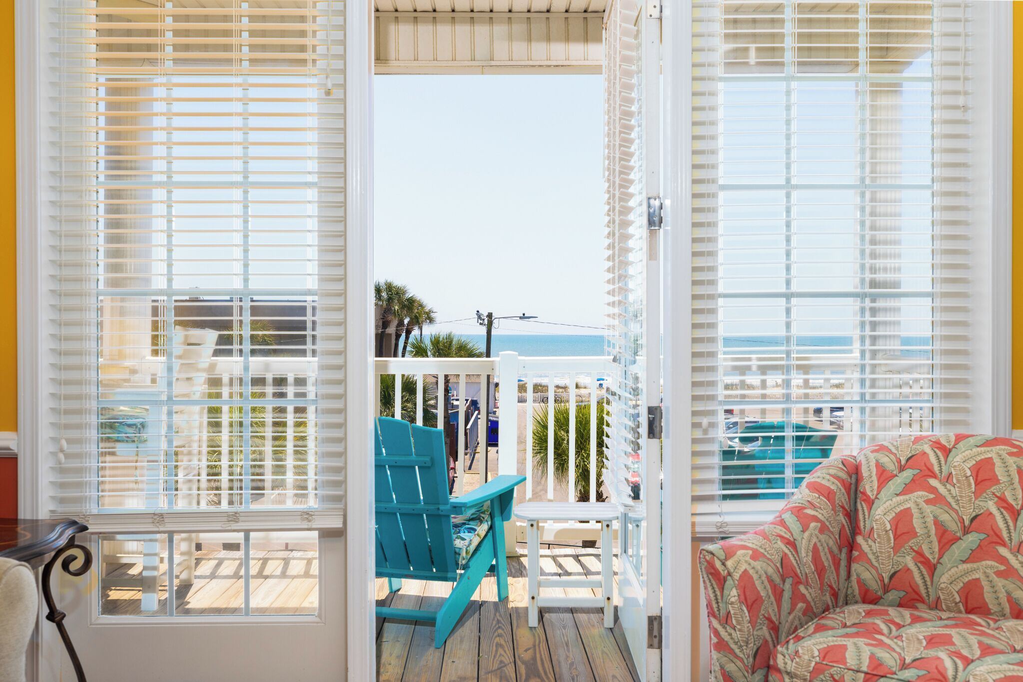 Une pièce avec vue sur l’océan, une terrasse en bois et une chaise turquoise.