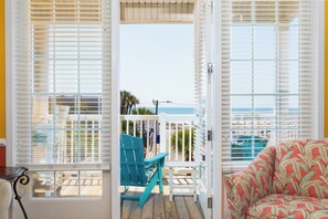 A room with a view of the ocean, a wooden deck, and a turquoise chair.