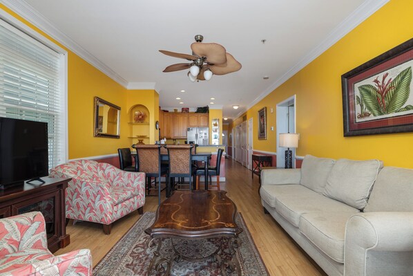 A living room with a sofa, chairs, a coffee table, a TV, and a ceiling fan.