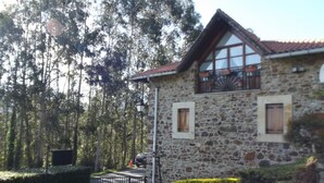 A stone building with a sloped roof and large windows, surrounded by a well-maintained garden and tall trees. - Rural house with garden and beautiful views (Sopuerta)