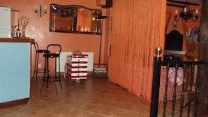 A room with a kitchen area, a dining table with chairs, a red and white striped cart, and a large window with curtains. - Rural house with garden and beautiful views (Sopuerta)