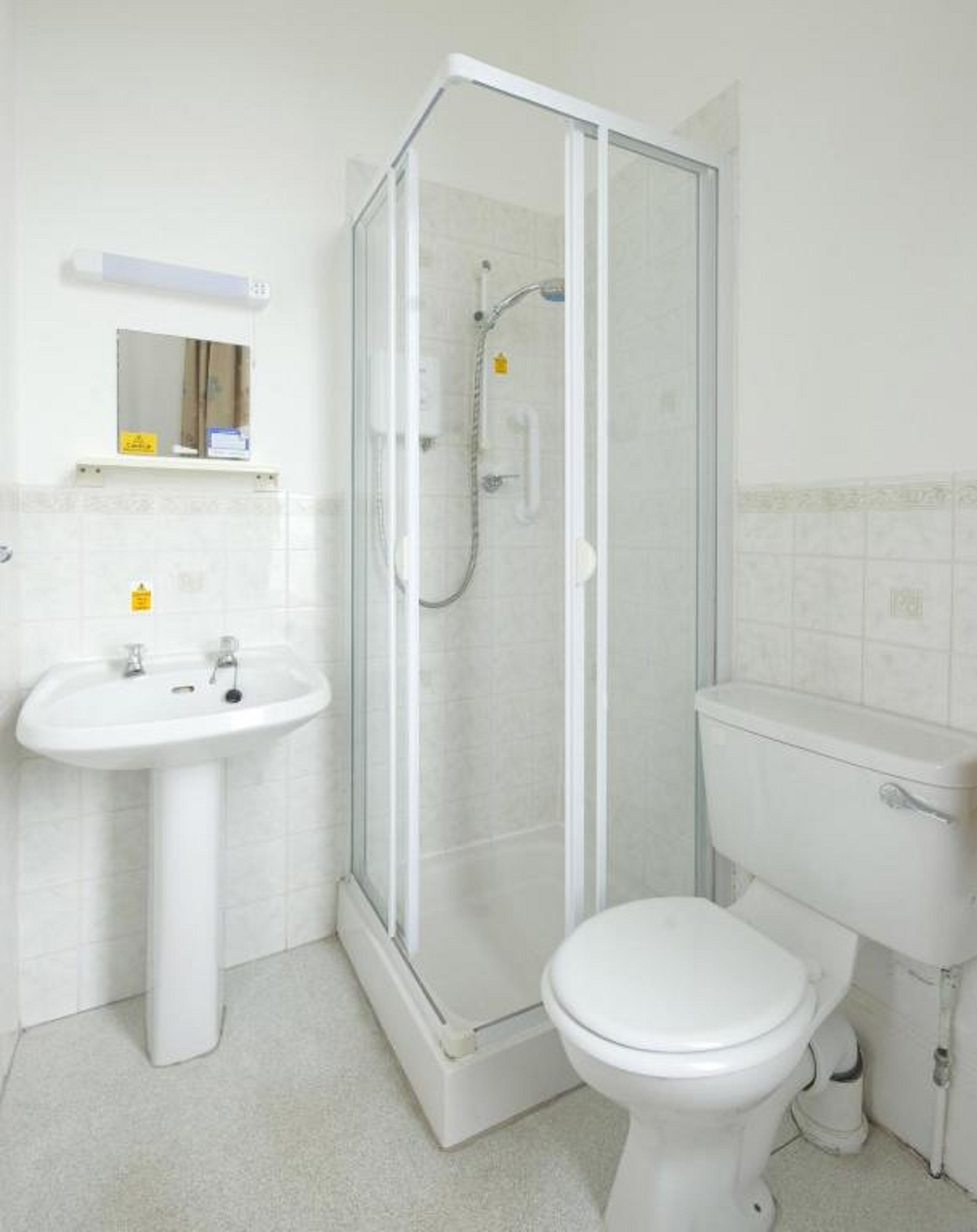 Une salle de bain avec une douche à parois de verre, un lavabo sur colonne et des toilettes.