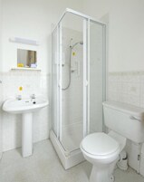 Un baño con ducha envuelta en vidrio, lavamanos pedestal y retrete.
