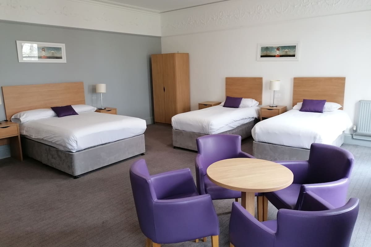 A hotel room with two beds, a wardrobe, a round table with chairs, and two bedside lamps.