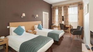 A hotel room with two beds, a desk, a chair, a TV, and a lamp. - The Caledonian Torbay Hotel (Torquay)