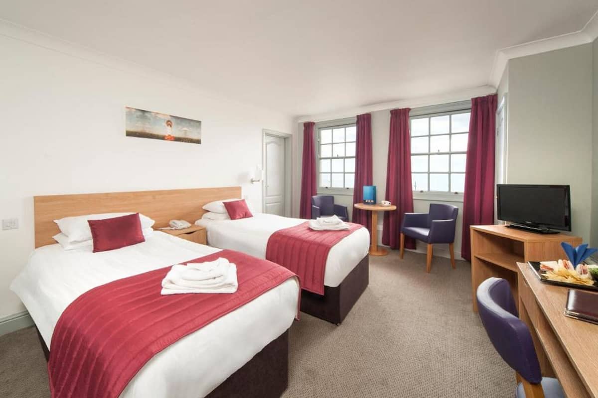 A hotel room with two beds, a desk, a chair, a television, and a window with curtains.