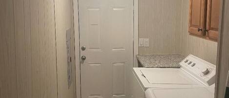A compact laundry room with a white washing machine and dryer, a small rug, and wooden cabinets.