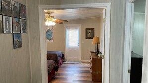Ein Flur, der in ein Schlafzimmer mit Deckenventilator, einer Tür mit Jalousien und einem Schminktisch mit Lampe führt.