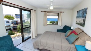 A bedroom with a bed, a window with a view, a ceiling fan, and a balcony.