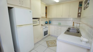 A compact kitchen with white cabinets, a refrigerator, a stove, and a sink.