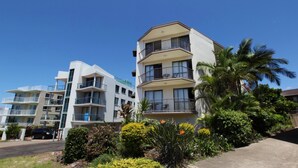 A multi-story residential building with balconies, surrounded by tropical vegetation.