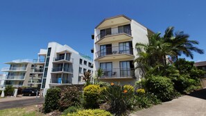 Un edificio residencial de varios pisos con balcones, rodeado de follaje tropical.
