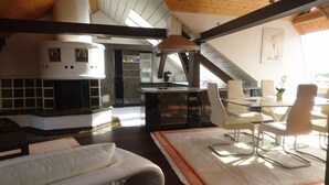 A modern kitchen with a central island, a dining area with a glass table and chairs, and a large window providing natural light. - Penthouse Himmelreich spacious 155 m² maisonette with fireplace & air conditioning (Senftenberg)