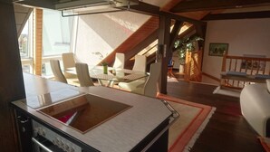 A modern kitchen with a large island, a dining area with glass tables and chairs, and a staircase leading to an upper level. - Penthouse Himmelreich spacious 155 m² maisonette with fireplace & air conditioning (Senftenberg)