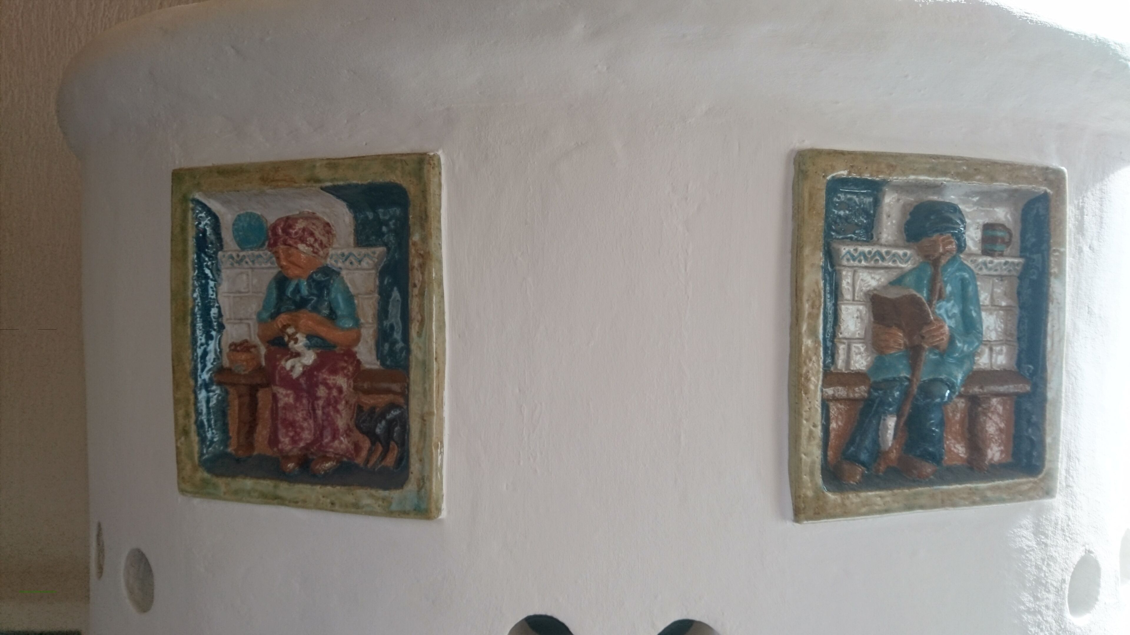 Deux panneaux, fixés au mur, représentent des silhouettes : l’un est assis et l’autre est debout, le tout sur un fond de mur uni.