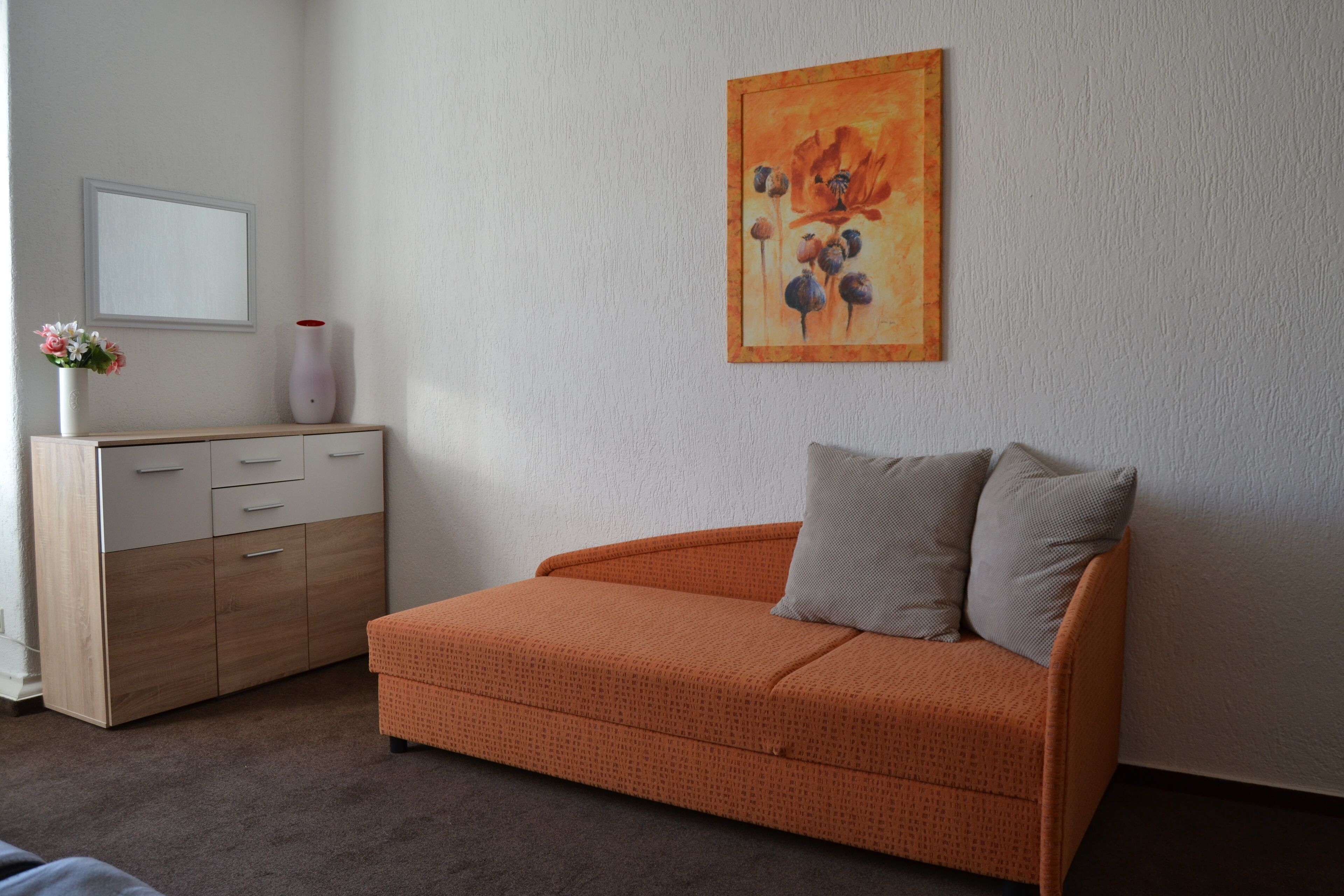A room with a wooden dresser, a grey sofa with two pillows, and a painting on the wall.