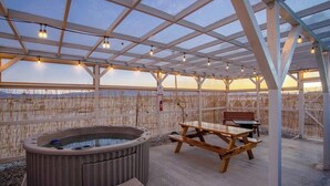 An outdoor patio with a hot tub, picnic table, and seating area, overlooking a scenic view.
