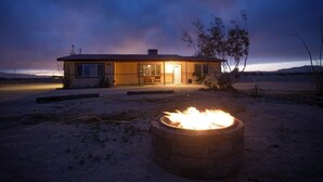 A house with a fire pit in the foreground and a porch with a bench.