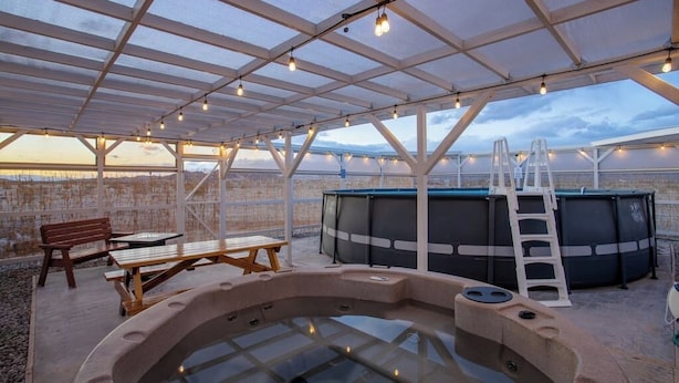 An outdoor hot tub area with a wooden bench, a picnic table, and a ladder leading to a large black hot tub.