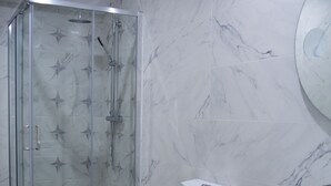 Et moderne badeværelse med bruseniche, toilet og vaskebord med spejl.