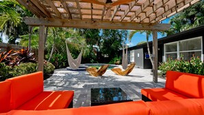 Ett takförsett utomhusområde med en pool, orange sittmöbler och en pergola av trä.