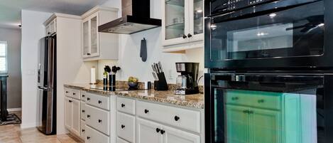 Une cuisine moderne avec des meubles blancs, un réfrigérateur en acier inoxydable, un four noir et un micro-ondes encastré.