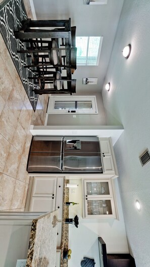 A modern kitchen with a stainless steel refrigerator, white cabinetry, and a granite countertop. - Barefoot Bungalow, Heated Pool & Spa, Game Room Foosball (Bradenton)