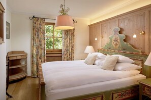 A bedroom with a wooden headboard, a bed with white linens, a hanging plant, and a window with curtains.
