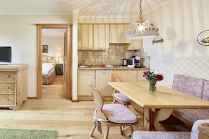 A cozy room with a wooden dining table, a sofa, and a kitchen area with wooden cabinets and a hanging light fixture. - Landsitz Romerhof (Kitzbühel)