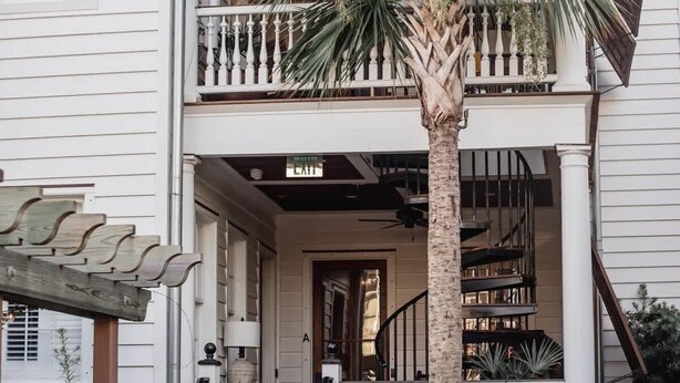 Ein zweistöckiges Haus mit Balkon, Treppe und einer Palme.