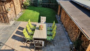 A patio with a wooden table and chairs, surrounded by a stone wall and a grassy area. - Gute Laune Hof Klingenthal (Klingenthal)