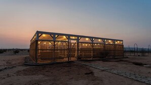 Een groot, rechthoekig gebouw met een metalen frame en glazen panelen, gelegen in een woestijnlandschap onder een heldere lucht.