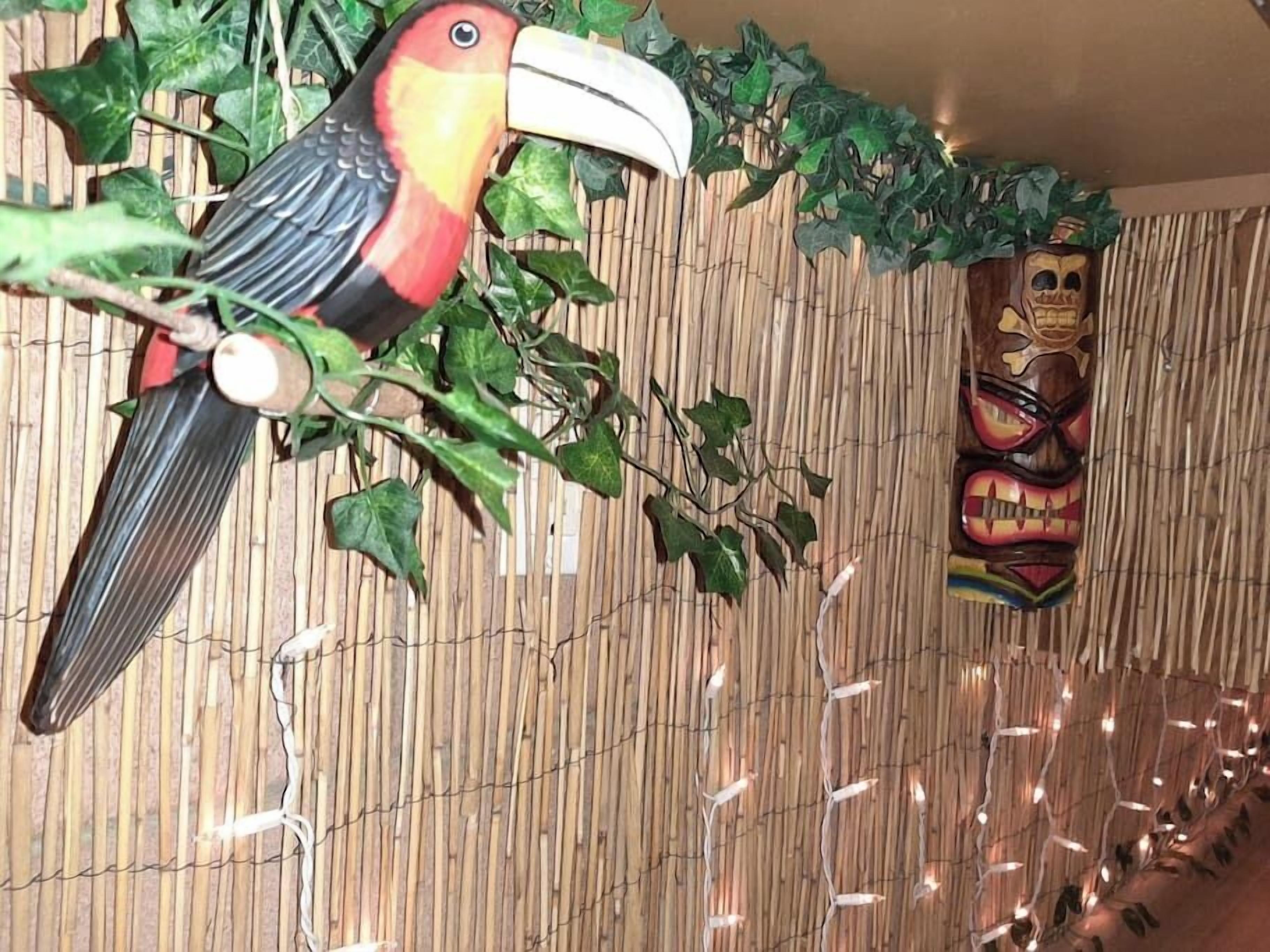 Una habitación con pared de bambú, un tucán decorativo y una máscara tiki.