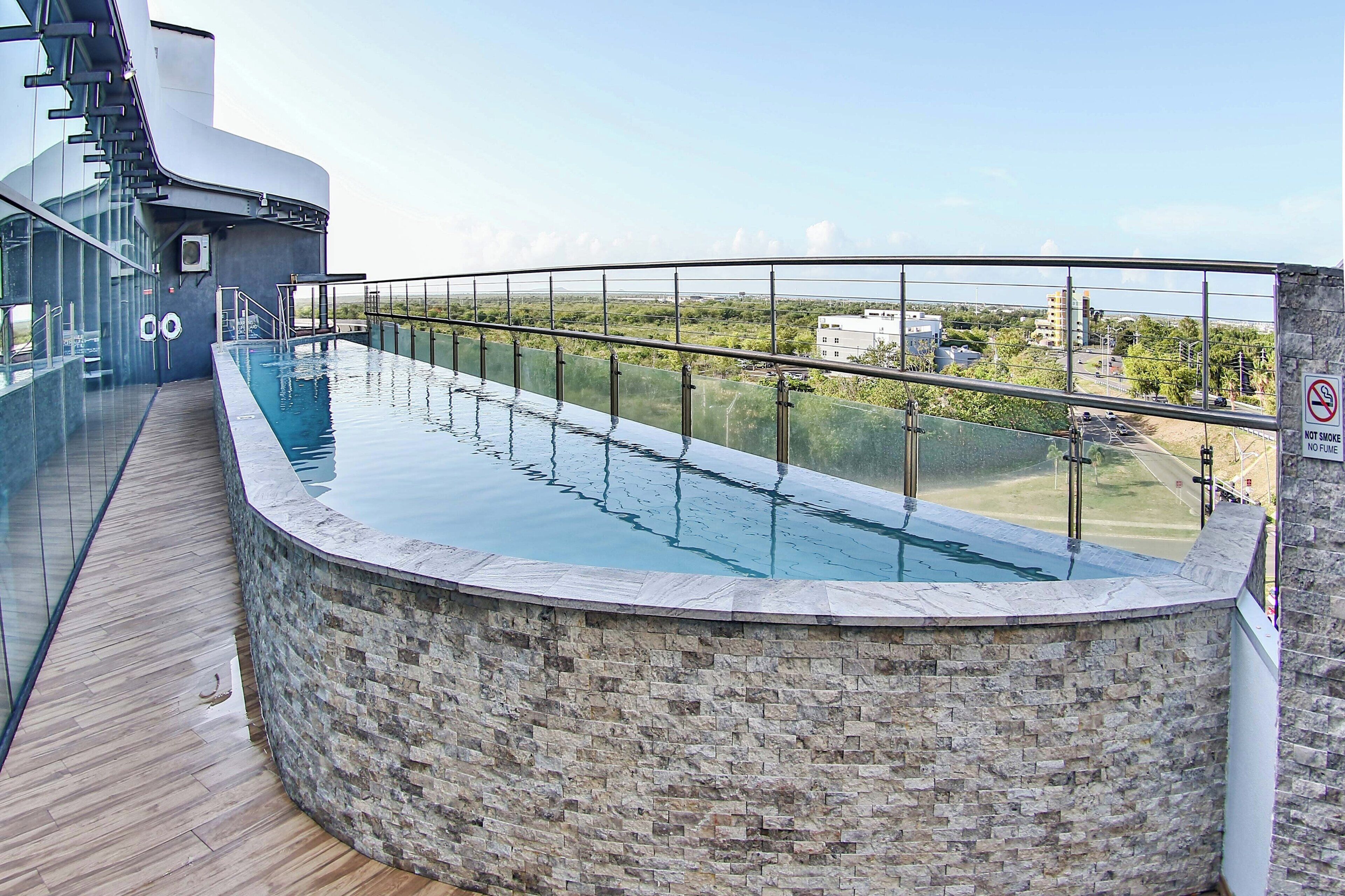 Una piscina moderna con una barrera de vidrio, un muro de piedra y vistas del paisaje circundante.