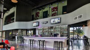 Un área de bar moderna con techo alto, barra, varios taburetes y un amplio ventanal con vistas al exterior.