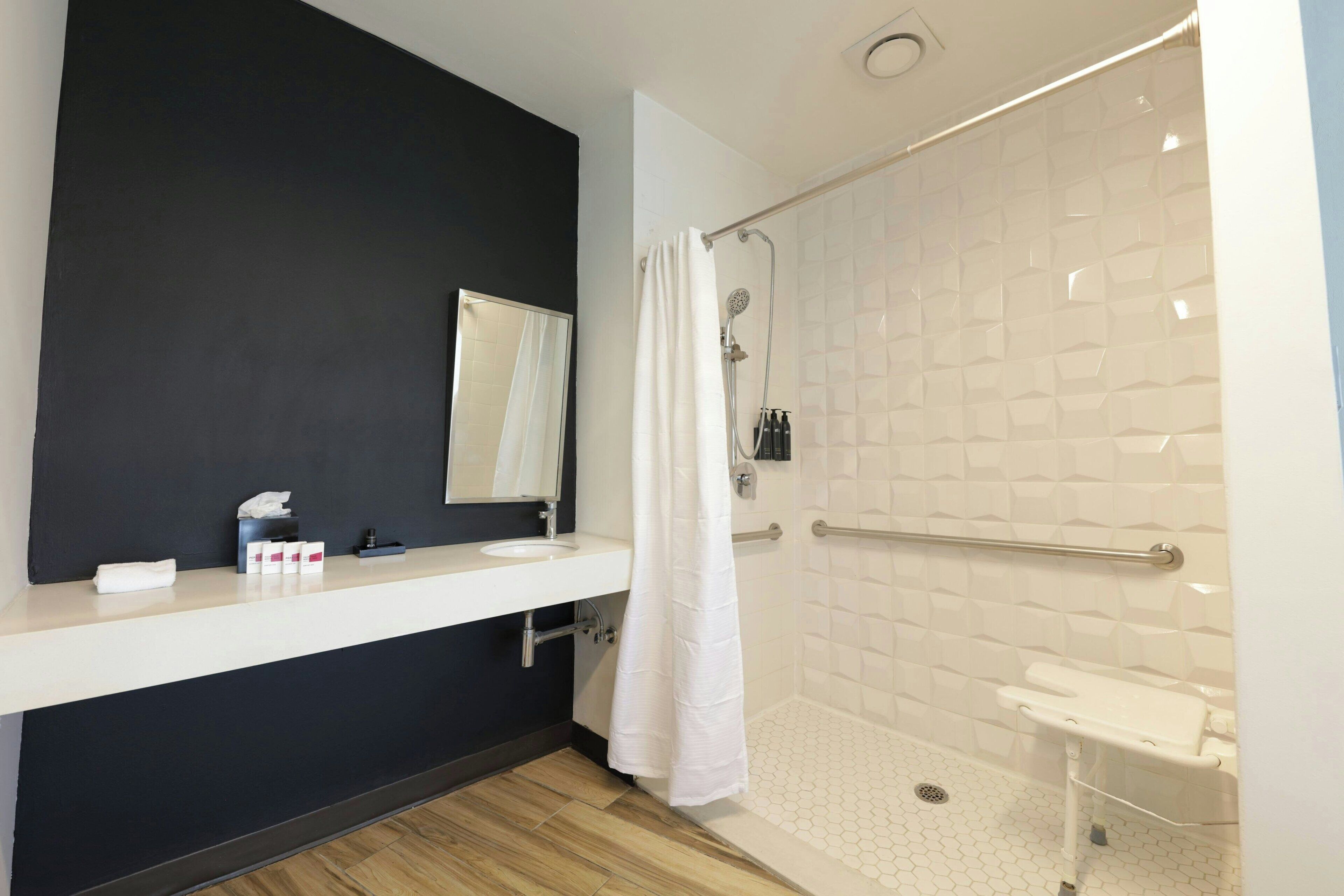 Un baño moderno con pared oscura, un lavabo blanco, un espejo y una ducha con cortina blanca.