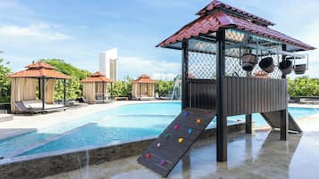 Piscina com escorregador de madeira e dois quiosques com telhados vermelhos.