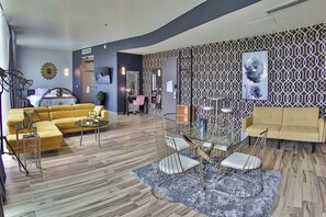 A modern living room with a yellow sofa, a glass coffee table, and a dining area with a glass table and metal chairs.