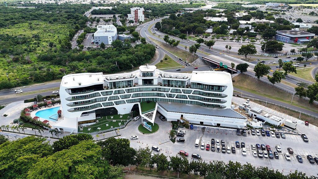 A modern building with a curved facade, a swimming pool, and a parking lot.