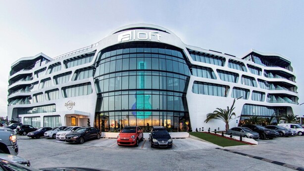 A modern hotel with a curved facade, multiple balconies, and a prominent 'aloft' sign.