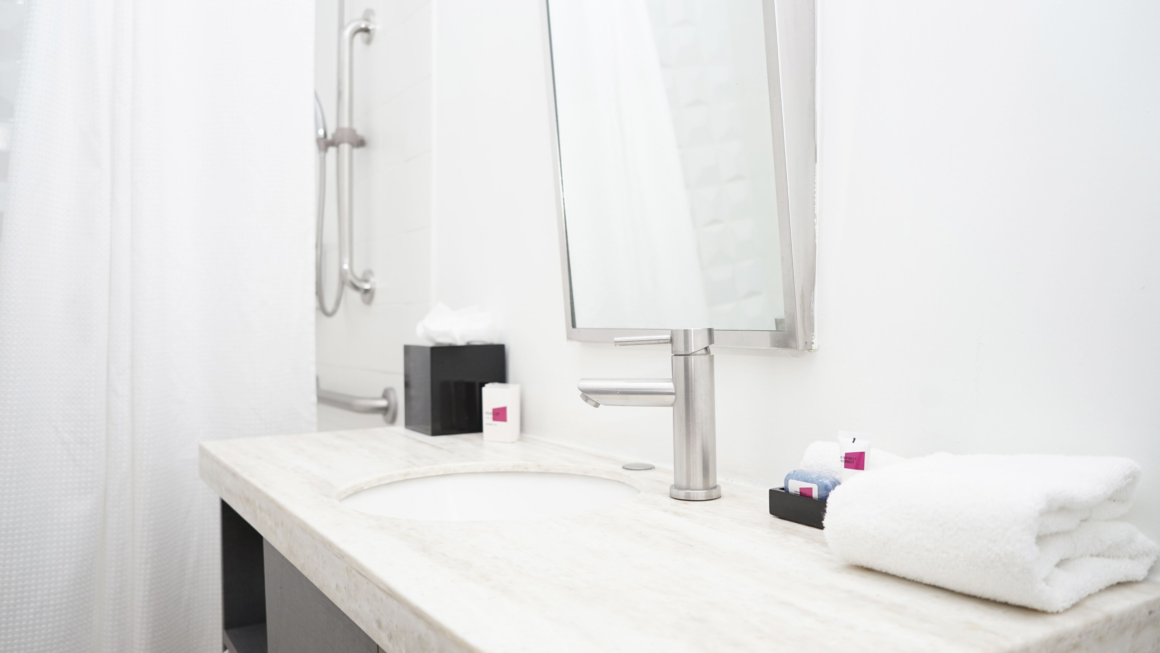 A bathroom with a white sink, a mirror, a towel, and a shower.